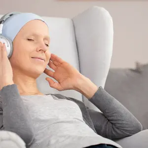 Peaceful woman with headphones and blue headscarf resting at home after cancer treatment Peaceful woman with headphones and blue headscarf resting at home after cancer treatment