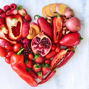 Collection of fresh red vegetables and fruits arranged in a heart shape on white rustic background strawberry raspberry pomegranate peppers capsicum chilli potato beans