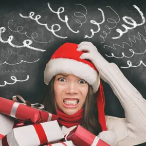 Christmas stress, woman in Santa hat stressed out, drawings of headache spirals on black blackboard 