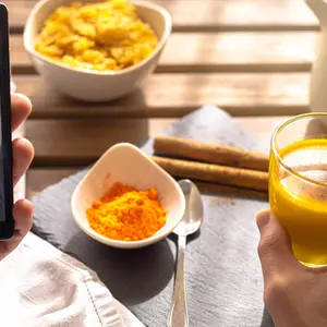 Selective focus of a person having breakfast with golden milk turmeric and Indian cinnamon for energy while looking at the cell phone a guy doing stretching and exercises 