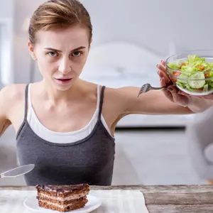 Depressed young woman refusing from the salad while wanting to eat the cake