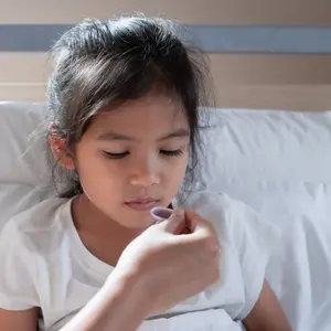 Asian mother giving cough syrup medicine on a spoon to her daughter in bed