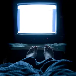 Person sleeps in his bed with TV on at night with his feet sticking up out of the blankets. 