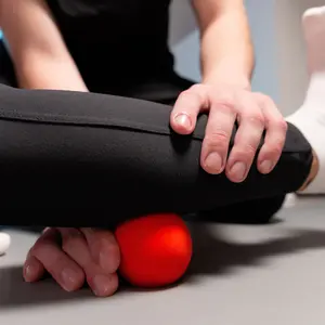 Close-up young male massage therapist teaches a woman myofascial self-massage using a massage ball indoors.