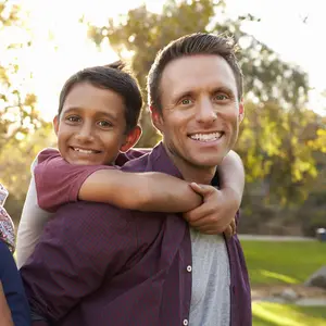 Mixed race parents carry their kids piggyback in a park