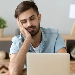 Exhausted millennial male hold head with hand sitting at office table falling asleep