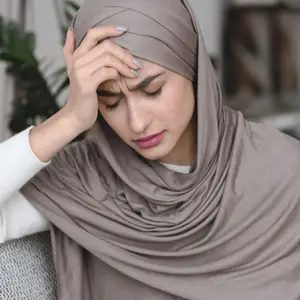 Muslim woman in headscarf sitting on sofa and touching head with headache