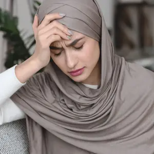 Muslim woman in headscarf sitting on sofa and touching head with headache Muslim woman in headscarf sitting on sofa and touching head with headache