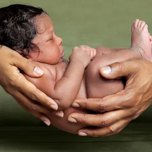 An isolated image of African American parent hands holding their newborn, baby girl in front of a green background.