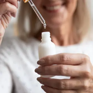Close up happy older woman opening bottle pipetting skincare product.