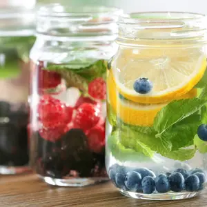 Mason jars of infused water with fruits and berries on wooden table