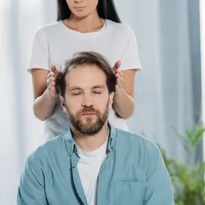 Bearded man with closed eyes sitting and receiving reiki treatment from young female healer