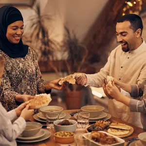 Happy Muslim parents and their kids sharing pita bread while eating dinner