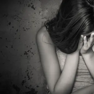 Black and white grunge image of a beautiful teenage girl sitting on the floor crying