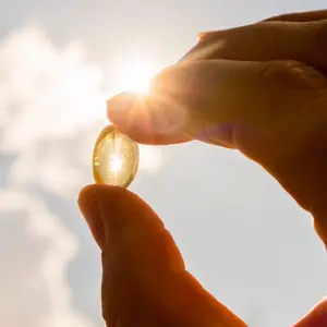 Yellow soft shell D-vitamin capsule against sun and blue sky on sunny day.