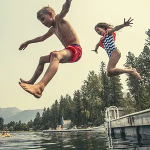 Kids jumping off the dock into a beautiful mountain lake. 
