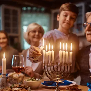 Close up of kid and his extended family lighting the menorah during dinner at dinning table on Hanukkah.