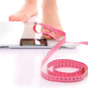 A picture of female feet standing on a bathroom scales and a tape measure over white background