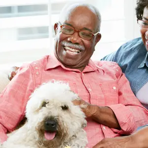 Happy Senior Couple Sitting On Sofa With Dog