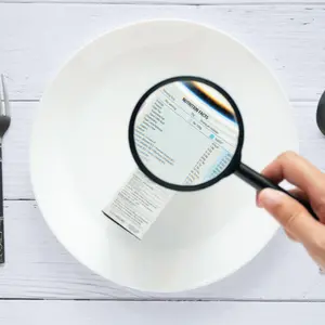 hand use the magnifying glass to zoom in to see the details of the nutrition facts label on the side of the consumer product box on white dish
