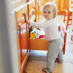 Toddler girl at home, opening the snack drawer in the kitchen and selecting food