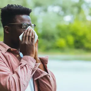 Man with seasonal allergies blowing on wipe in a park on spring day