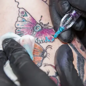 Tattoo artist applies light blue color to a tattoo