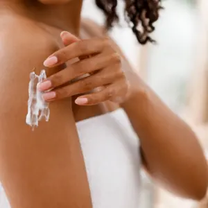 Black woman applying moisturizing lotion on body after shower