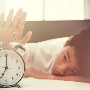 Alarm clock and sleepy teenage boy with hand reaching out for alarm clock
