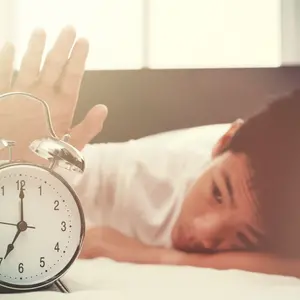 Alarm clock and sleepy teenage boy with hand reaching out for alarm clock Alarm clock and sleepy teenage boy with hand reaching out for alarm clock