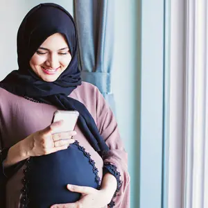 Young pregnant arab woman in hijab using her mobile phone