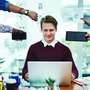 A man at his computer surrounded by extended arms representing stressors