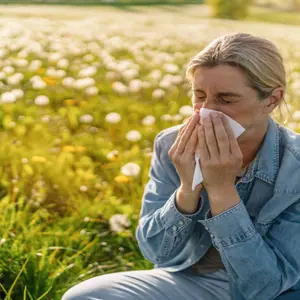 Woman blowing her nose while sitting in a grassy field