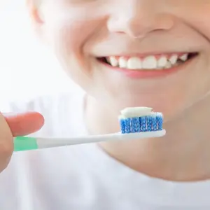 The boy is holding a toothbrush in his hands, brushing teeth with fluoride-toothpaste