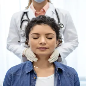 Endocrinologist examining throat of young woman in clinic. 