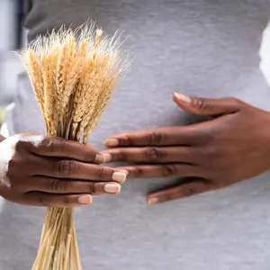 Black woman holding a handful of wheat and her belly, signifying celiac disease and gluten intolerance