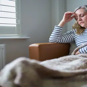 woman sitting on the couch rubbing her head in pain/fatigue, suffering from long COVID