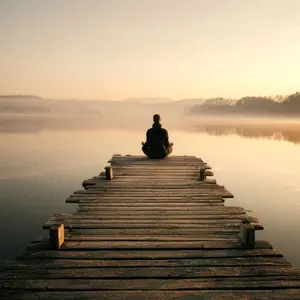 Person meditating in a sitting position at the end of a dock on a lake at dawn