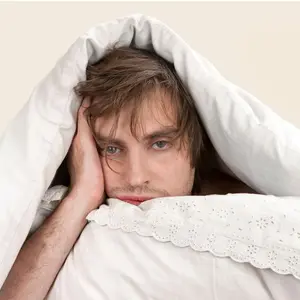 Tired man in bed with covers over his head