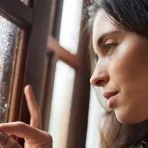 Melancholic woman looks out winter window