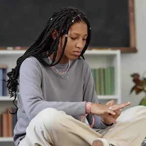 image of Black teenaged girl sitting cross-legged on desk waiting in school library during break