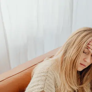 blonde woman sick on couch, holding her head