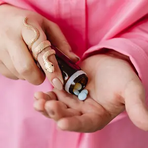 woman in pink shirt emptying medication pills into hands