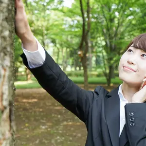 businesswoman on cell phone, raising hand to touch tree, smiling